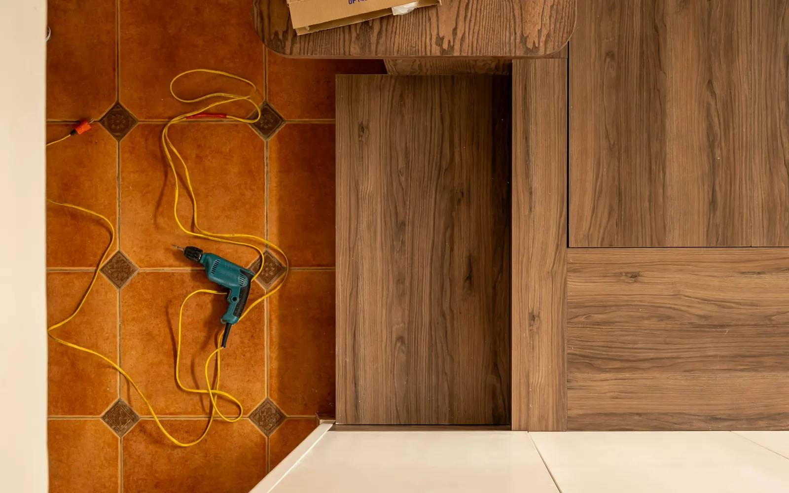 Flooring installation area with wood flooring, a drill, and a power cord.